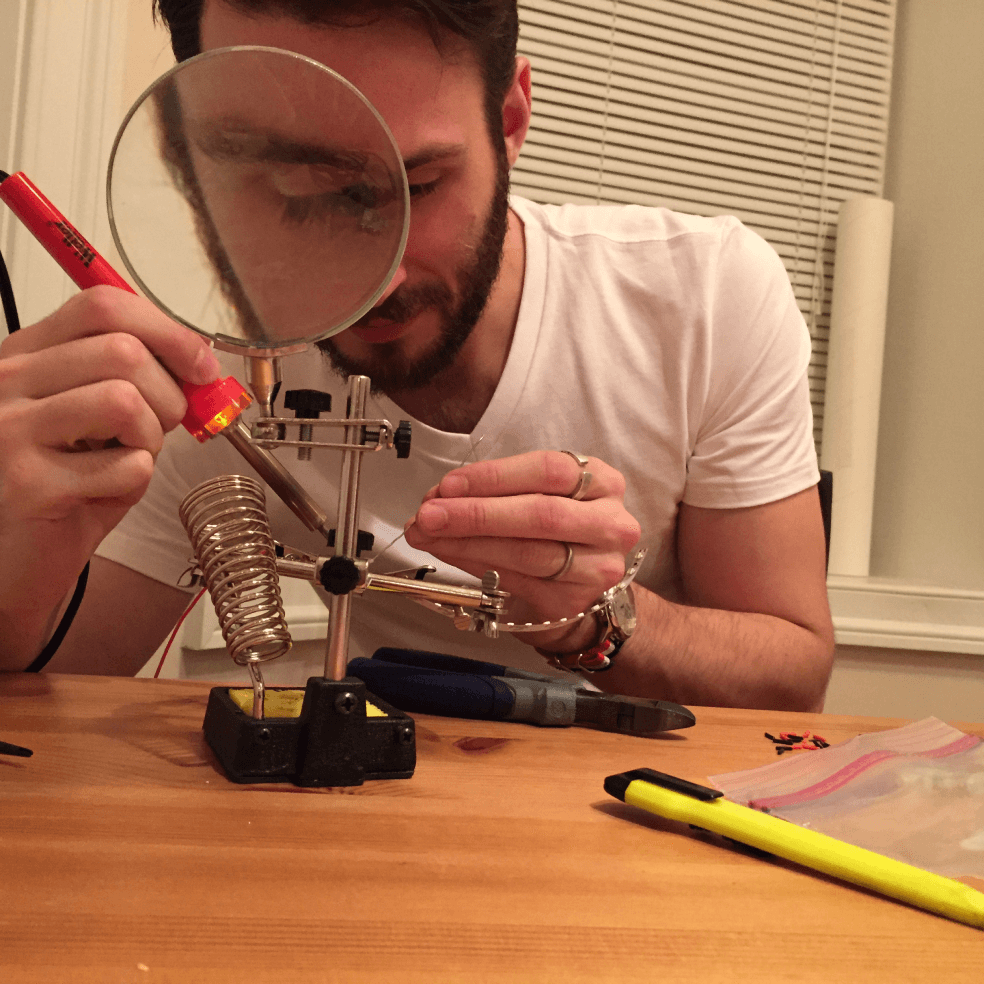 Photo of Alex Jacque soldering a component from the MICA Grad Show sign